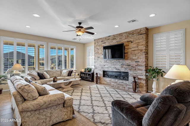 tiled living room featuring ceiling fan and a stone fireplace