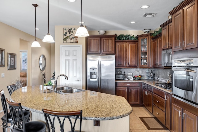 kitchen with sink, a breakfast bar area, hanging light fixtures, stainless steel appliances, and a kitchen island with sink