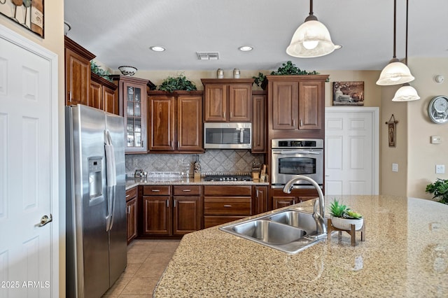 kitchen with appliances with stainless steel finishes, tasteful backsplash, sink, hanging light fixtures, and light tile patterned floors