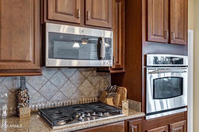 kitchen with appliances with stainless steel finishes, light stone counters, and decorative backsplash