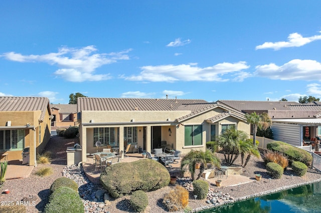 rear view of property with a patio, a tiled roof, a water view, fence, and stucco siding