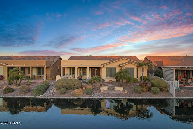 rear view of house featuring a patio, a water view, and stucco siding