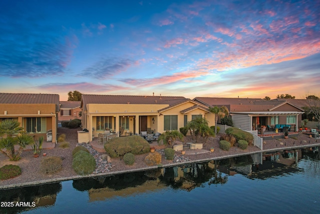 back of property featuring a water view, a patio area, and stucco siding