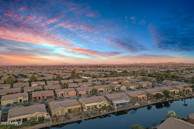 aerial view at dusk with a water view and a residential view