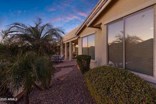 property exterior at dusk featuring a patio area and stucco siding