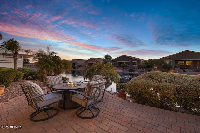 patio terrace at dusk featuring a water view and a fire pit