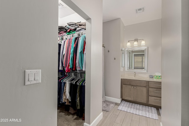 bathroom featuring baseboards, visible vents, wood finished floors, a spacious closet, and vanity