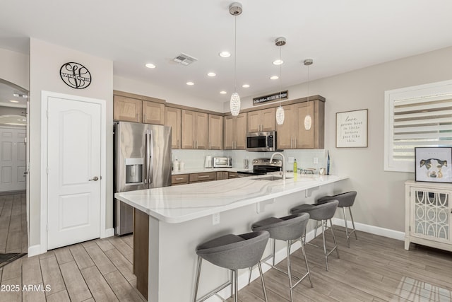 kitchen featuring a peninsula, visible vents, a kitchen breakfast bar, appliances with stainless steel finishes, and backsplash