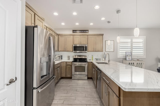 kitchen featuring light stone counters, stainless steel appliances, backsplash, a sink, and a peninsula