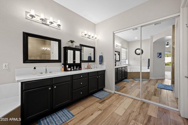 full bath featuring visible vents, a sink, wood finished floors, double vanity, and ceiling fan