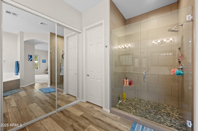 bathroom featuring visible vents, a stall shower, a washtub, and wood finished floors