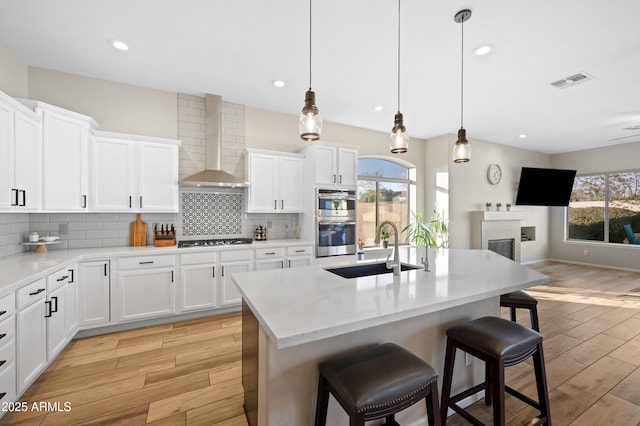 kitchen with visible vents, a sink, tasteful backsplash, stainless steel appliances, and wall chimney exhaust hood