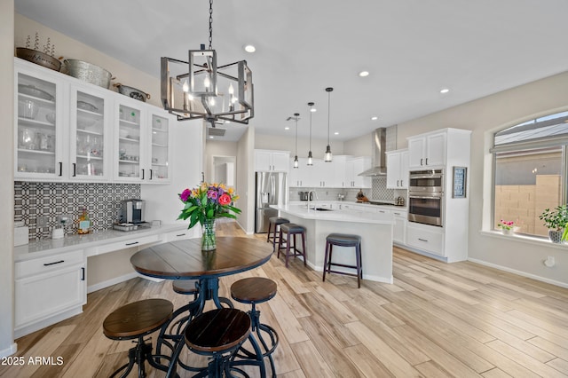 kitchen with light wood-type flooring, a kitchen breakfast bar, stainless steel appliances, and wall chimney exhaust hood