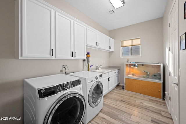 laundry room featuring visible vents, light wood finished floors, cabinet space, a sink, and independent washer and dryer