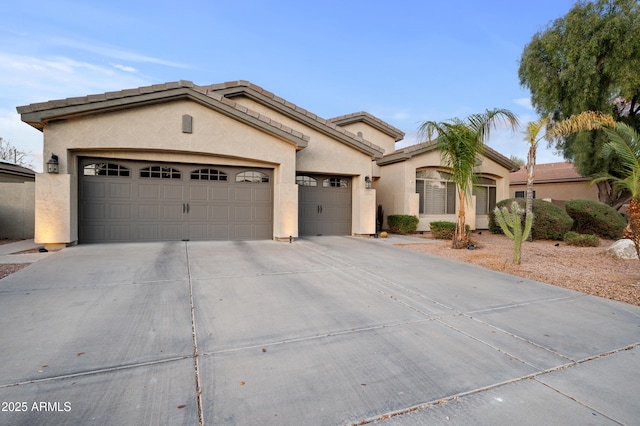 mediterranean / spanish house with stucco siding, concrete driveway, an attached garage, and a tile roof