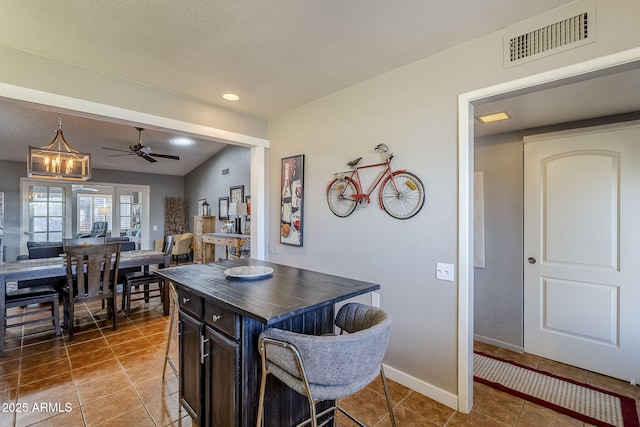 kitchen with wooden counters, a textured ceiling, a kitchen island, ceiling fan with notable chandelier, and tile patterned floors