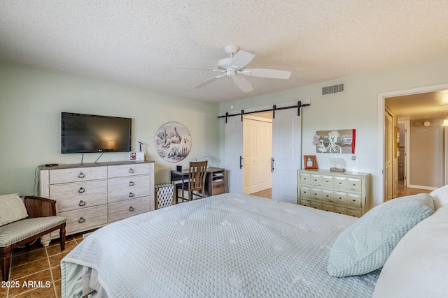 tiled bedroom with ceiling fan, a barn door, and a textured ceiling