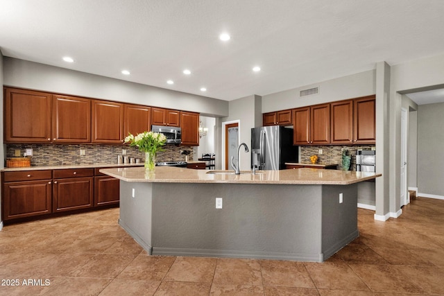 kitchen with light stone countertops, stainless steel appliances, sink, a kitchen island with sink, and light tile patterned floors