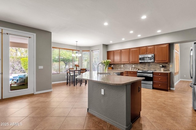 kitchen with pendant lighting, stainless steel appliances, an island with sink, backsplash, and light tile patterned floors