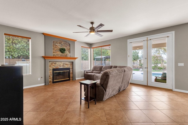 tiled living room featuring ceiling fan, french doors, a wealth of natural light, and a stone fireplace