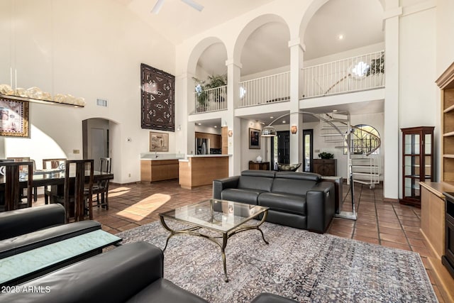 living area with visible vents, a ceiling fan, tile patterned floors, stairs, and high vaulted ceiling