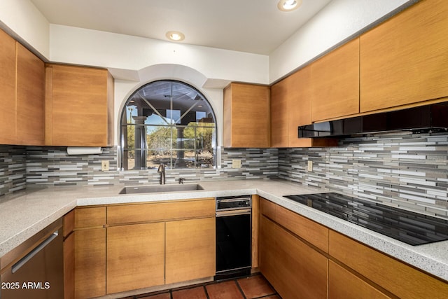 kitchen featuring a sink, black electric stovetop, light countertops, under cabinet range hood, and backsplash