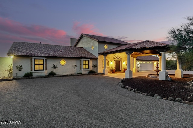 rear view of property with driveway, a tiled roof, an attached garage, and stucco siding