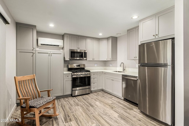 kitchen featuring light wood finished floors, stainless steel appliances, light countertops, an AC wall unit, and a sink