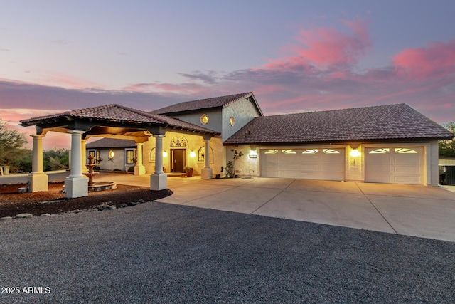 mediterranean / spanish home featuring central air condition unit, driveway, an attached garage, and stucco siding