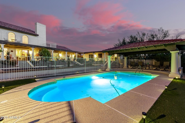 pool at dusk with a patio area, fence, a fenced in pool, and a gazebo