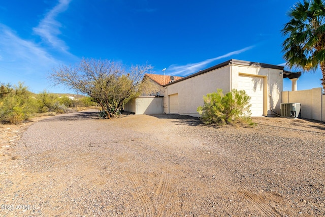 view of side of home featuring driveway, an attached garage, fence, and stucco siding