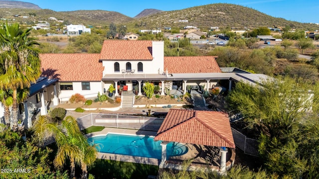 rear view of house with a balcony, a fenced backyard, a chimney, a patio area, and a mountain view