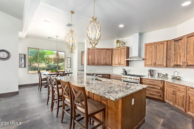 kitchen featuring pendant lighting, a kitchen island with sink, wall chimney range hood, stainless steel stove, and a notable chandelier