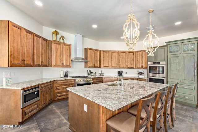 kitchen featuring an inviting chandelier, a center island with sink, wall chimney range hood, hanging light fixtures, and appliances with stainless steel finishes