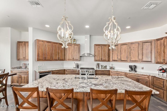 kitchen featuring sink, an island with sink, wall chimney range hood, and an inviting chandelier