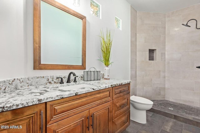 bathroom featuring a tile shower, vanity, and toilet