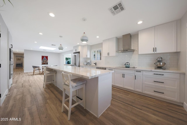 kitchen with visible vents, a kitchen island, appliances with stainless steel finishes, wood finished floors, and wall chimney exhaust hood