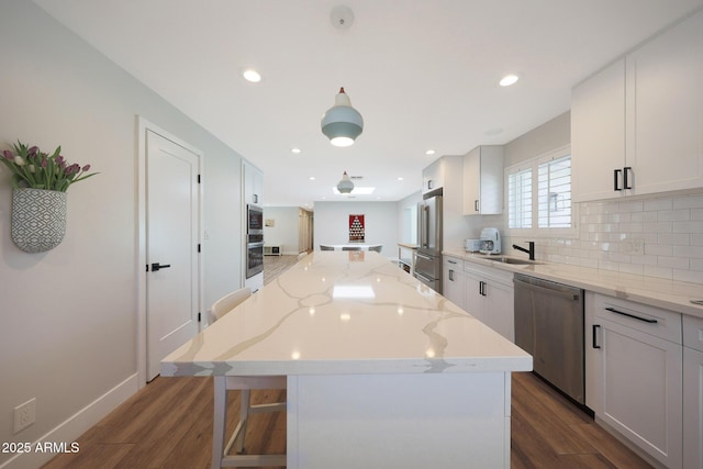 kitchen featuring dark wood-type flooring, a sink, tasteful backsplash, a center island, and stainless steel appliances