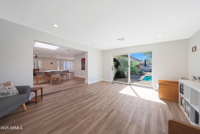 living room with light wood-type flooring, visible vents, recessed lighting, a skylight, and baseboards