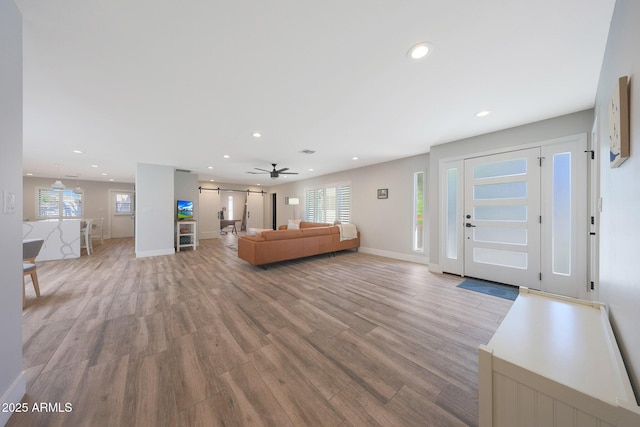 unfurnished living room featuring recessed lighting, light wood-style flooring, baseboards, and a barn door