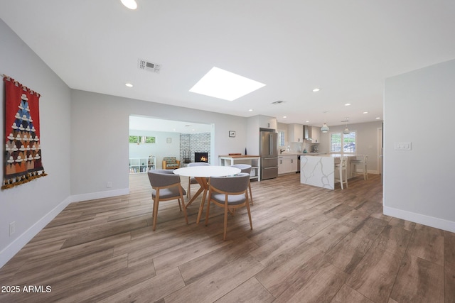 dining area with visible vents, light wood-style flooring, a warm lit fireplace, and baseboards