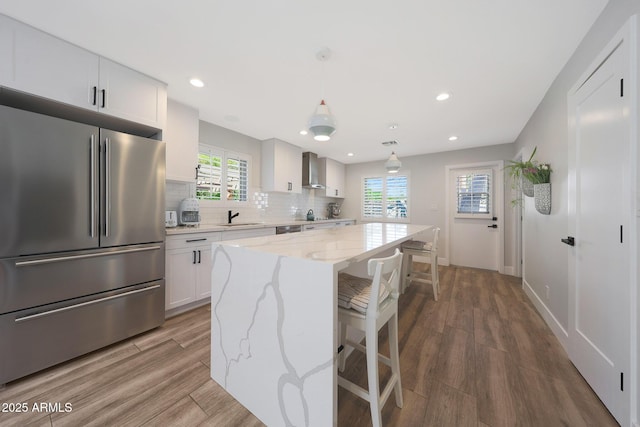 kitchen featuring tasteful backsplash, wall chimney range hood, wood finished floors, stainless steel fridge, and a sink