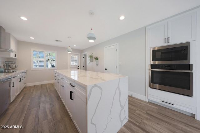 kitchen with light stone counters, white cabinets, a center island, and wood finished floors