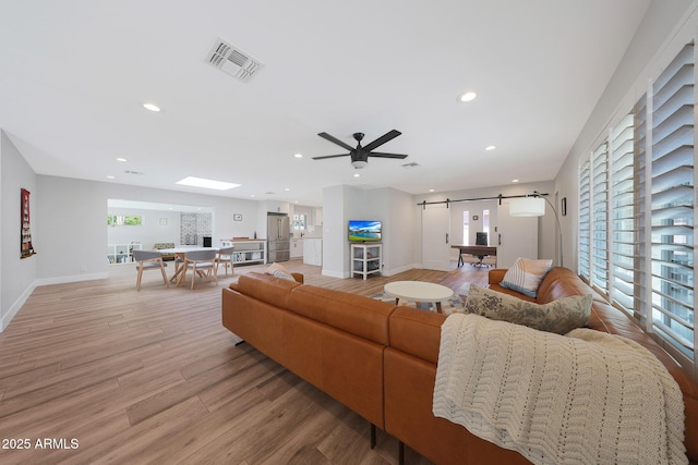 living area featuring visible vents, recessed lighting, a barn door, light wood finished floors, and baseboards