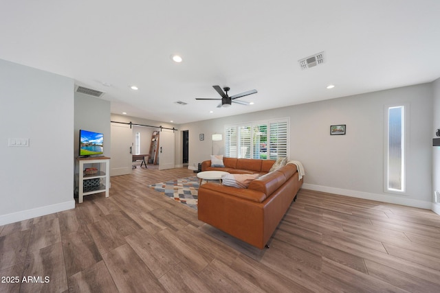 living room with a barn door, wood finished floors, visible vents, and baseboards