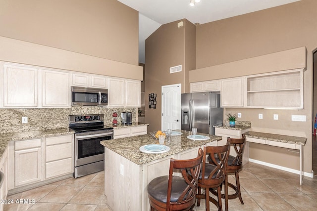 kitchen with a kitchen breakfast bar, light stone counters, stainless steel appliances, a kitchen island, and light tile patterned flooring