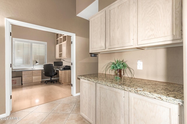 kitchen featuring light brown cabinets, built in desk, light tile patterned floors, and light stone counters