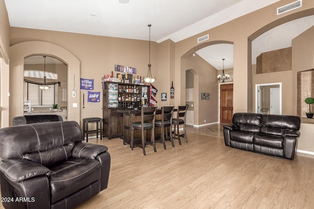 living room with bar area, light hardwood / wood-style flooring, and an inviting chandelier