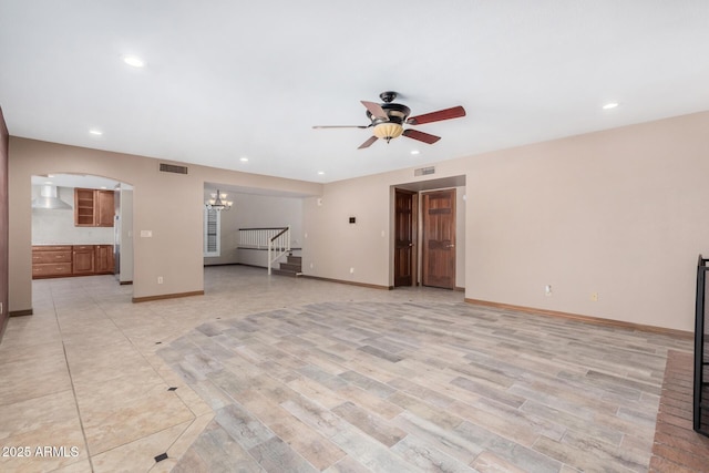 unfurnished living room with visible vents, stairway, baseboards, and ceiling fan with notable chandelier