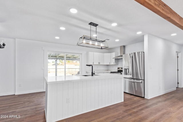 kitchen featuring appliances with stainless steel finishes, wall chimney exhaust hood, decorative light fixtures, white cabinetry, and an island with sink